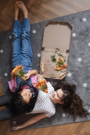 Foto de Amigos felices tumbados en el suelo y comiendo una pizza. - Imagen libre de derechos