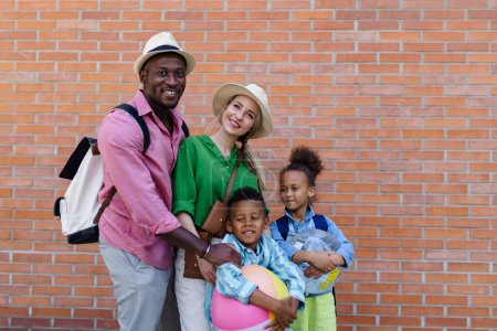 Photo for Multiracial family travelling together with small kids. Posing in front of a brick wall with beach ball. - Royalty Free Image