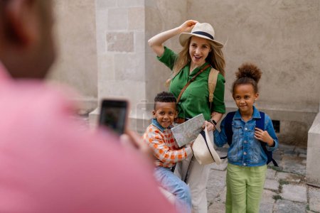 Téléchargez les photos : Famille multiraciale voyageant avec de jeunes enfants. Prendre une photo dans la vieille ville cetre. - en image libre de droit