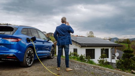 Téléchargez les photos : Homme d'affaires mature attendant de charger sa nouvelle voiture électrique. - en image libre de droit