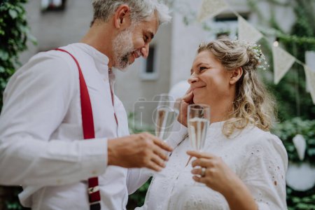 Foto de A mature bride and groom toasting at wedding reception outside in the backyard. - Imagen libre de derechos