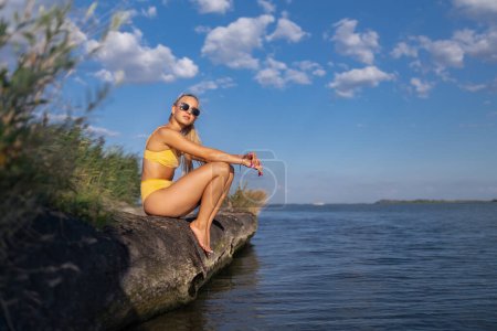Photo for Young woman in a swimsuit sitting at lake, summer vacation concept. - Royalty Free Image
