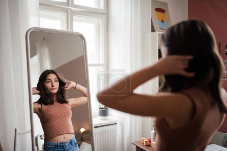 Téléchargez les photos : Jeune adolescente regardant dans le miroir dans la chambre. - en image libre de droit