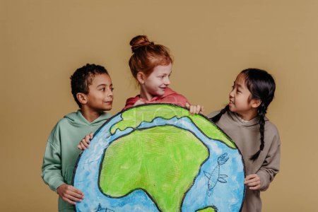 Foto de Retrato de tres niños con modelo de Tierra, sesión de estudio. Concepto de diversidad en una amistad. - Imagen libre de derechos