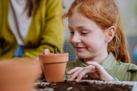 Foto de Niña feliz mirando la planta en crecimiento en una olla de cerámica. - Imagen libre de derechos