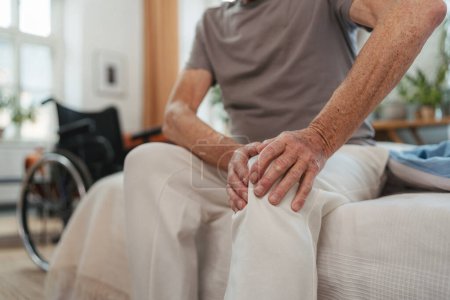 Foto de Primer plano del hombre mayor con dolor de rodilla sentado en la cama. - Imagen libre de derechos