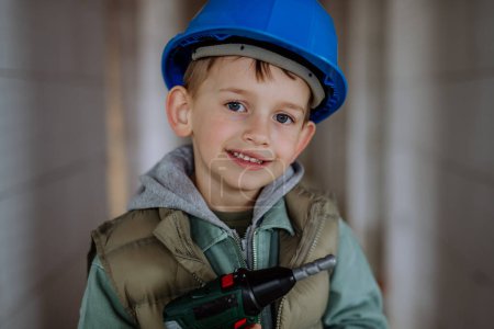 Téléchargez les photos : Portrait d'un petit garçon dans une maison inachevée posant avec casque et perceuse. - en image libre de droit
