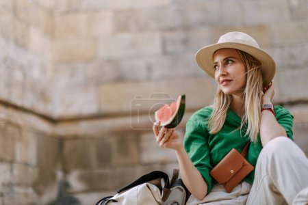 Photo for A young woman traveller eating watermelon in street during hot sunny day, summer vacation trip concept. - Royalty Free Image