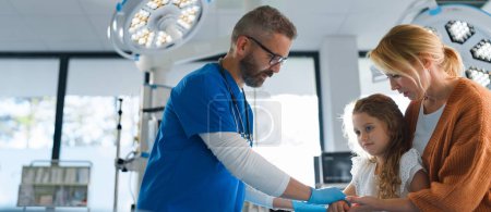 Photo for Mature doctor giving gypsum to little girl on her broken arm. - Royalty Free Image