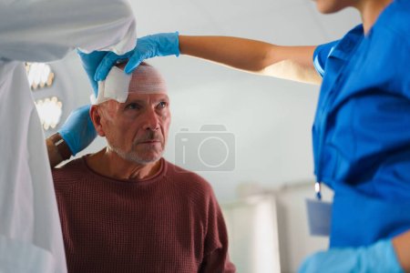 Téléchargez les photos : Gros plan du médecin et de l'infirmière traitant la tête blessée d'un aîné. - en image libre de droit