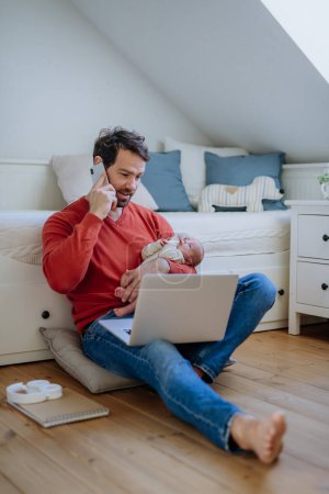 Foto de Padre sosteniendo a su bebé recién nacido llorando durante el trabajo en una computadora portátil. - Imagen libre de derechos