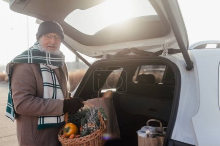 Téléchargez les photos : Senior homme donnant son achat dans le coffre de la voiture électrique. - en image libre de droit