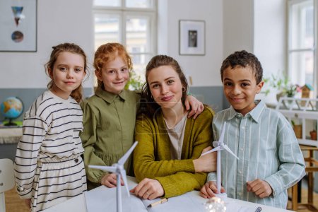 Photo for Young teacher with model of wind turbine learning her pupils about wind energy. - Royalty Free Image