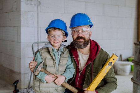 Téléchargez les photos : Portrait de père et son petit fils dans leur maison inachevée avec casque et outils. - en image libre de droit