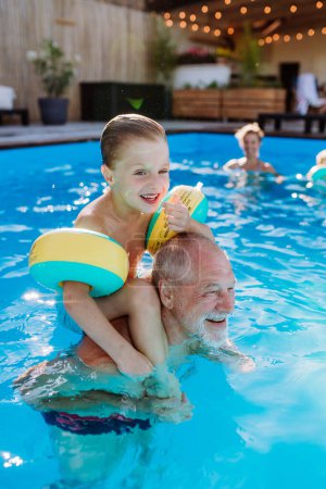 Foto de Un abuelo con su nieto divirtiéndose juntos al jugar en la piscina en el patio trasero. - Imagen libre de derechos