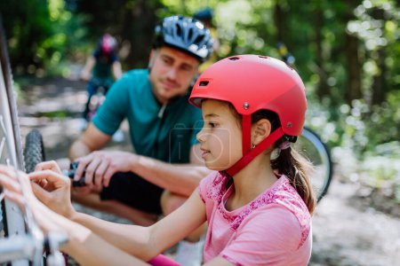Téléchargez les photos : Père vérifiant vélo à sa fille lors d'un voyage en famille dans une nature. - en image libre de droit