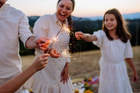 Foto de Happy family with children having picnic in the park, clebrating with sparklers. - Imagen libre de derechos