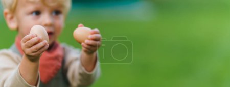 Téléchargez les photos : Portrait d'un petit garçon heureux tenant des œufs frais dans le jardin. - en image libre de droit