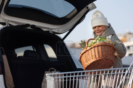Téléchargez les photos : Femme âgée donnant son achat dans le coffre de la voiture électrique. - en image libre de droit