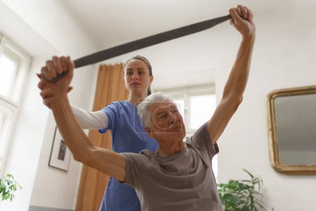 Photo for Young nurse doing exercise with senior man in his home. - Royalty Free Image