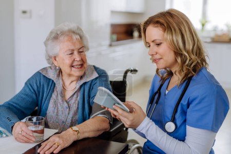Foto de Enfermera midiendo presión arterial a mujer mayor en su casa. - Imagen libre de derechos