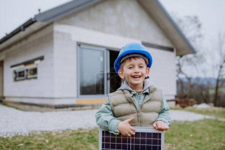 Foto de Retrato de un niño sosteniendo el panel solar, frente a su nueva casa sin terminar. - Imagen libre de derechos