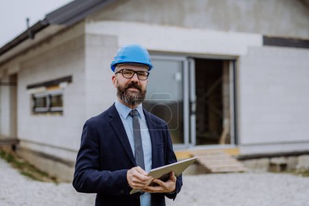 Photo for Mature businessman controlling blueprints from an unfinished house. - Royalty Free Image