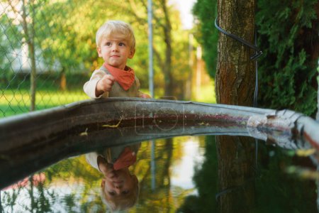 Téléchargez les photos : Joyeux petit garçon près du réservoir d'eau dans le jardin. - en image libre de droit