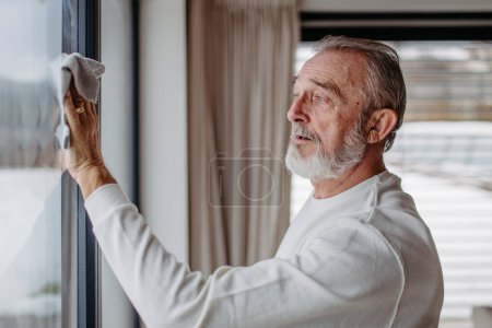 Téléchargez les photos : Senior homme nettoyer les fenêtres dans son appartement.. - en image libre de droit