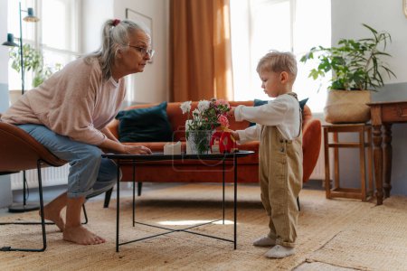 Téléchargez les photos : Grand-mère jouant avec son petit-fils dans le salon. Jouer avec camion de pompiers en bois rouge. - en image libre de droit