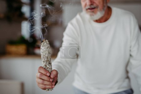Téléchargez les photos : Homme âgé faisant un rituel avec un sage dans sa maison. - en image libre de droit