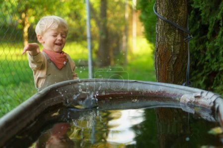 Téléchargez les photos : Joyeux petit garçon jetant des pierres dans le réservoir d'eau de pluie dans le jardin. Pierre sauter jeu. - en image libre de droit