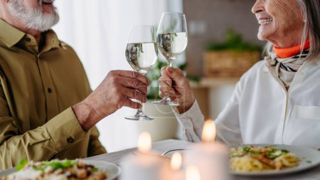 Téléchargez les photos : Senior avec sa femme pour fêter son anniversaire. Couple de personnes âgées ayant un dîner romantique, faire des acclamations avec des verres à vin. - en image libre de droit