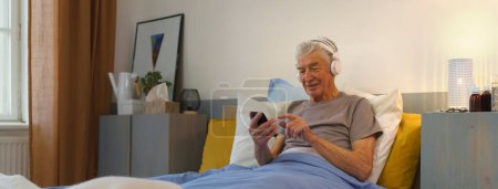 Photo for Senior man lying in a bed and enjoying music trough headphones. - Royalty Free Image