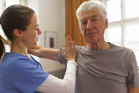 Foto de Enfermera joven haciendo ejercicio con un hombre mayor en su casa. - Imagen libre de derechos