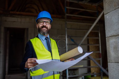Téléchargez les photos : Homme d'affaires mature contrôlant les plans d'une maison inachevée. - en image libre de droit