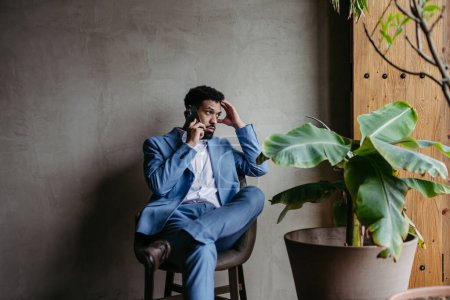 Foto de Retrato de un joven empresario sentado cerca de la ventana en una oficina verde llena de plantas. - Imagen libre de derechos