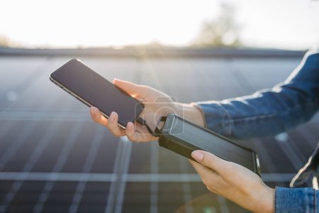 Photo for Close up of a woman charging her phone with solar charger on the roof with photovoltaics panels. - Royalty Free Image