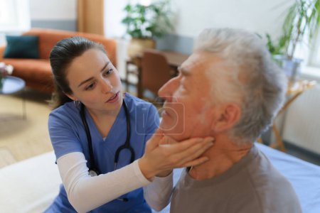 Photo for Doctor examine neck lymph nodes. Young nurse taking care of elderly senior in his home. - Royalty Free Image