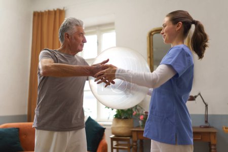 Photo for Young nurse doing exercise with senior man in his home. Young physiotherapist helping senior man to do exercise with fit ball, gymanstic ball. - Royalty Free Image
