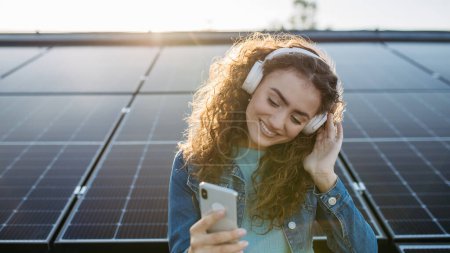 Foto de Retrato de mujer joven excitada, propietario en la azotea con paneles solares, escuchando música. - Imagen libre de derechos