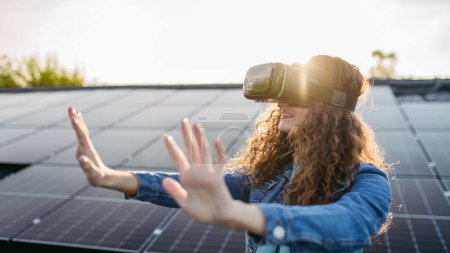 Photo for Young woman with virtual goggles on a roof with solar panels. - Royalty Free Image