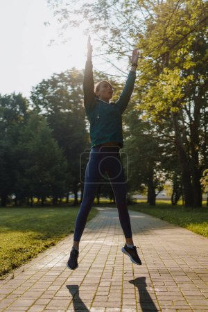 Photo for Fitness young woman doing full-body crossfit outdoor workout in the city park. Girl doing jumping jacks, star jumps exercise. - Royalty Free Image