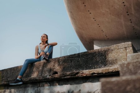 Photo for Young fitness woman resting after workout session in the city. Beautiful sporty woman enjoying sunrise after morning excercise. - Royalty Free Image