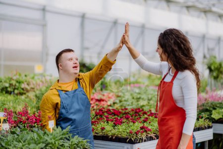 Foto de Una florista experimentada ayudando a una joven empleada con síndrome de Down en el centro de jardinería. - Imagen libre de derechos