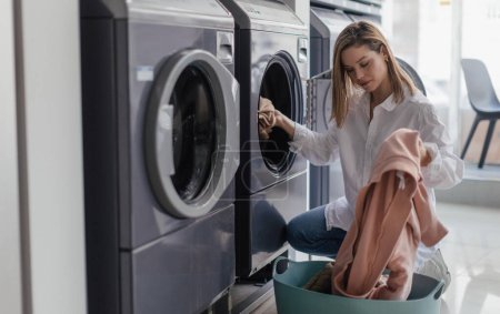 Junge Frau lädt Waschmaschine in öffentliche Wäscherei.