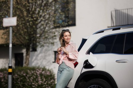 Foto de Mujer joven cargando coche eléctrico en el hogar, concepto de transporte sostenible y económico. - Imagen libre de derechos