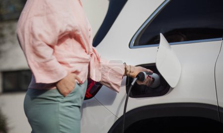 Primer plano de la mujer sosteniendo el cable de alimentación de su coche, cargándolo, concepto de transporte sostenible y económico.