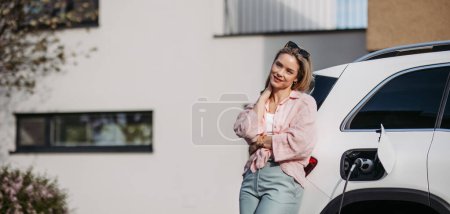 Photo for Young woman charging electric car in home, sustainable and economic transportation concept. - Royalty Free Image