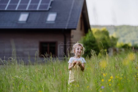 Foto de Retrato de una niña frente a una casa familiar con paneles solares, concepto de estilo de vida sostenible y recursos renovables. - Imagen libre de derechos